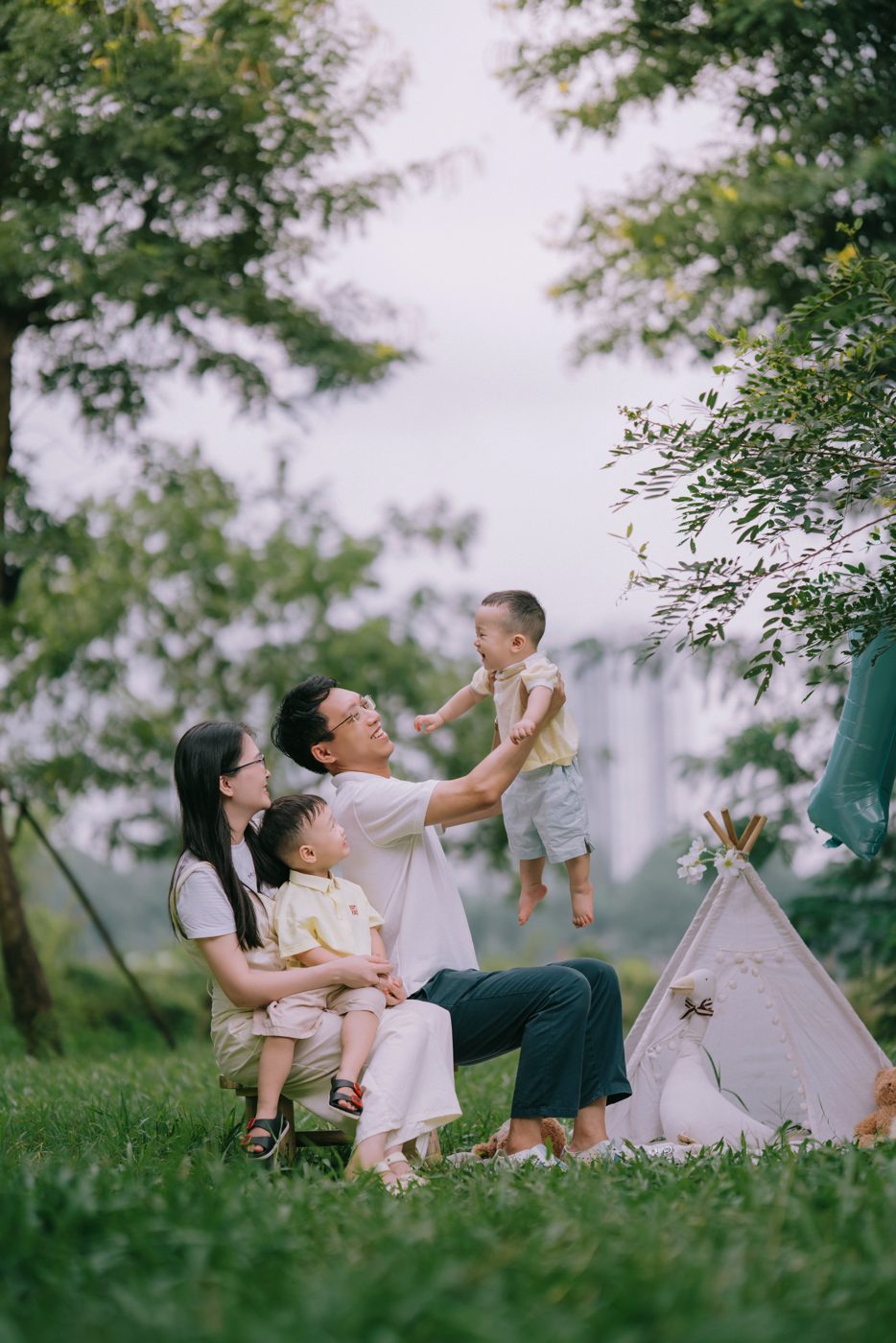 Bố tung bé út lên cao, mẹ ôm bé lớn trên bãi cỏ