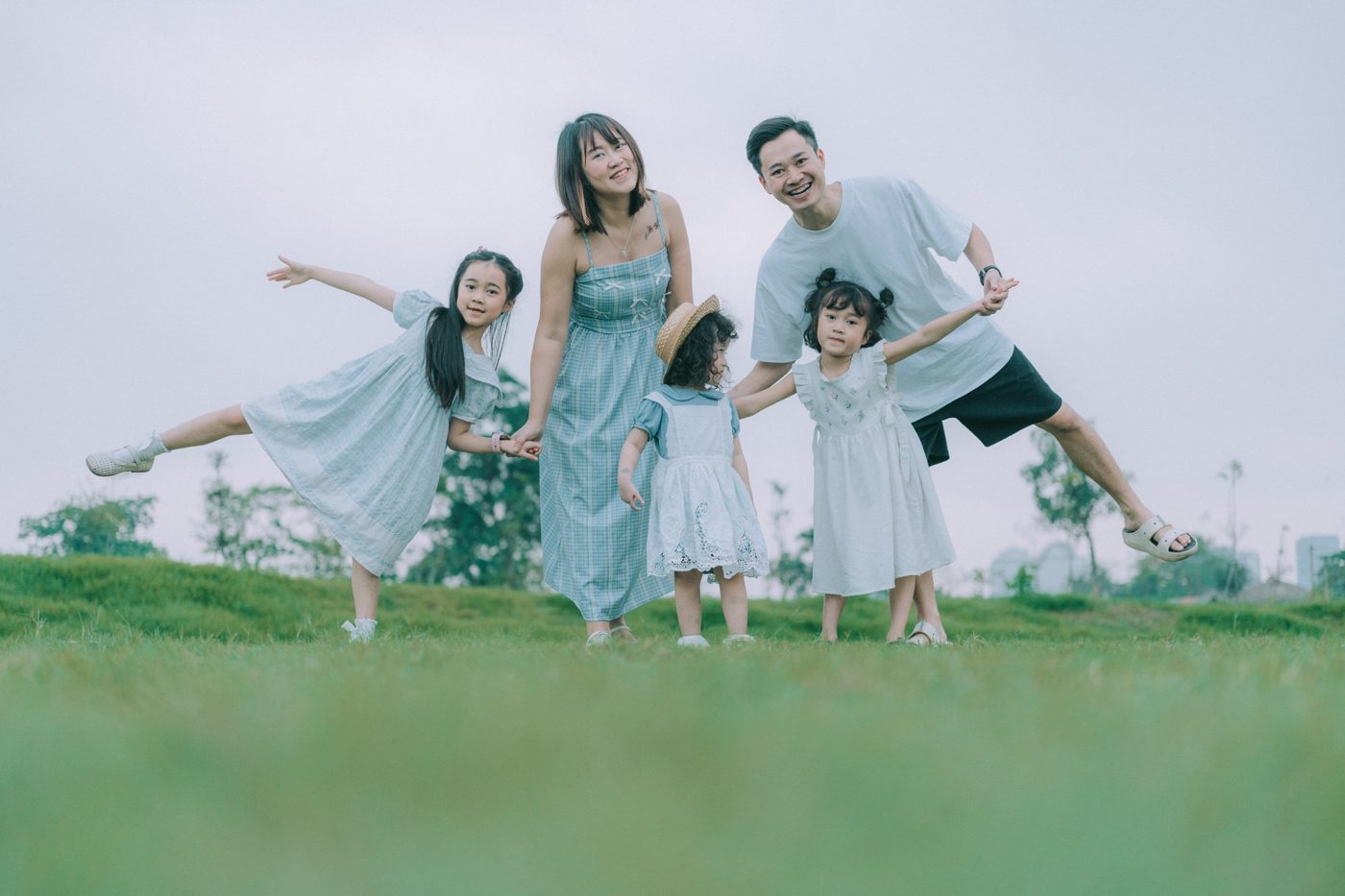 Bố mẹ và ba bé gái tạo dáng vui nhộn trên đồi cỏ