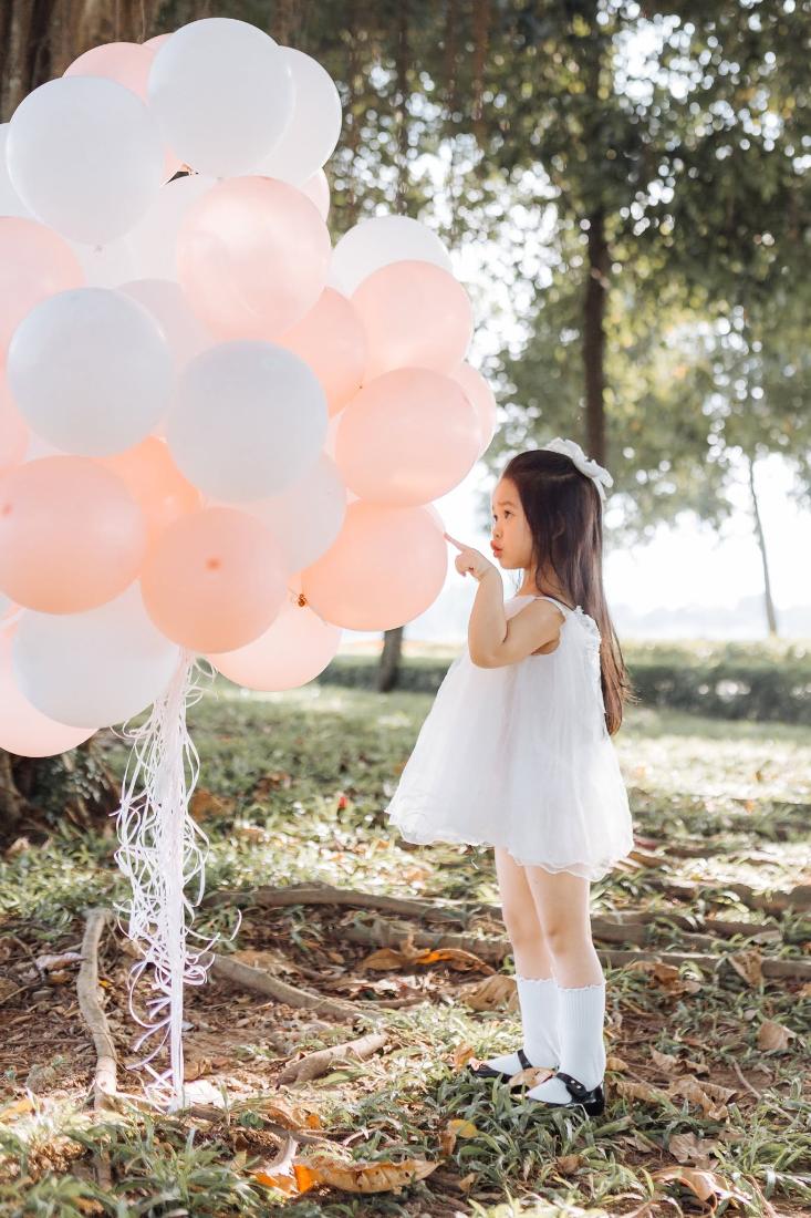 Bé gái váy trắng bên chùm bóng bay hồng