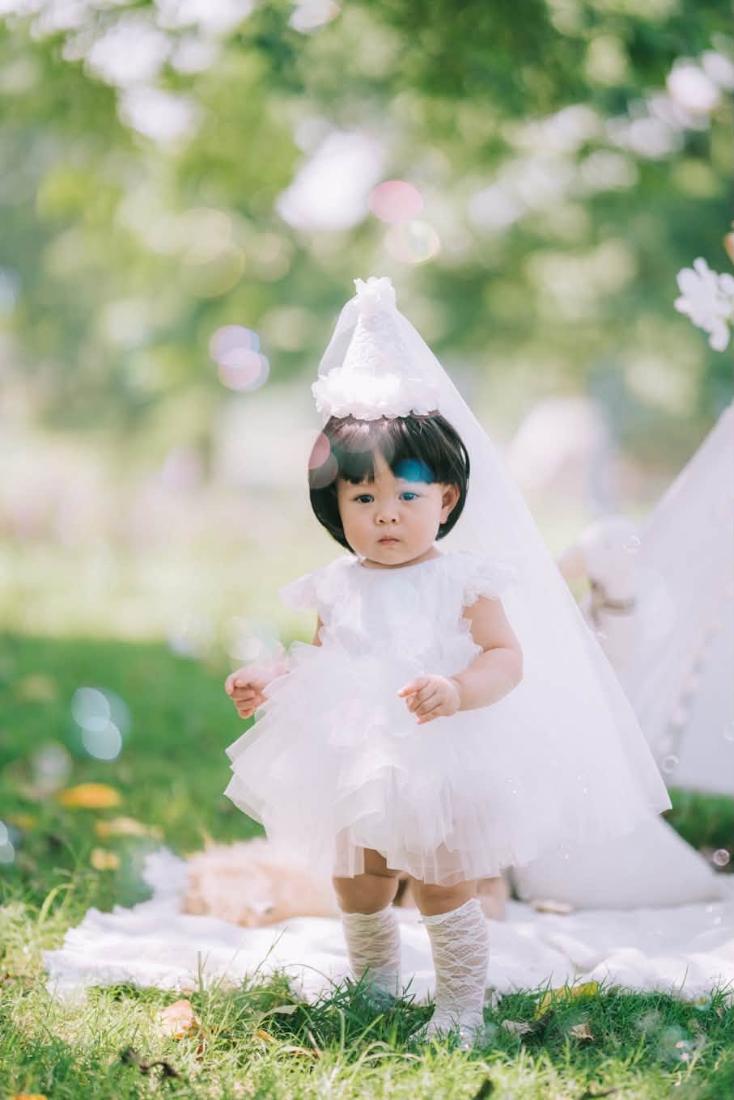 Bé mặc váy tutu trắng đứng trên bãi cỏ